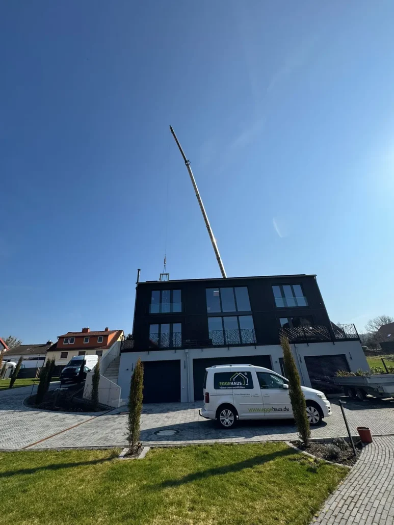 Fertiggestelltes Wohnhaus mit dunkler Fassade und Kran im Hintergrund